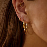 Close-up of an ear wearing gold hoop earrings with a blurred background