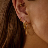 Close-up of an ear wearing gold hoop earrings with a blurred background