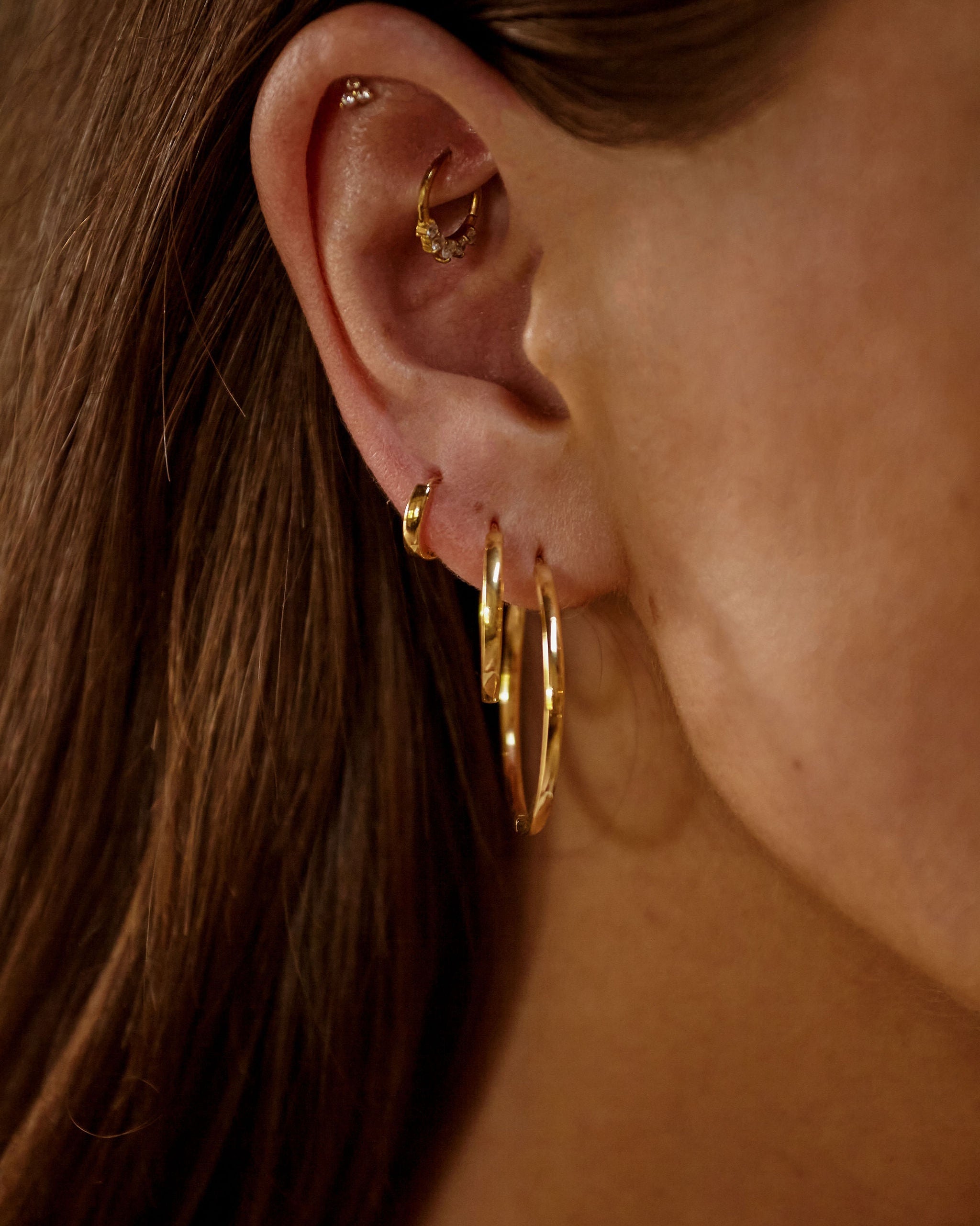 Close-up of an ear wearing gold hoop earrings with a blurred background
