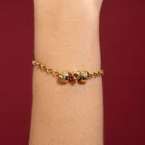 Gold bracelet with heart-shaped charms on a wrist against a red background