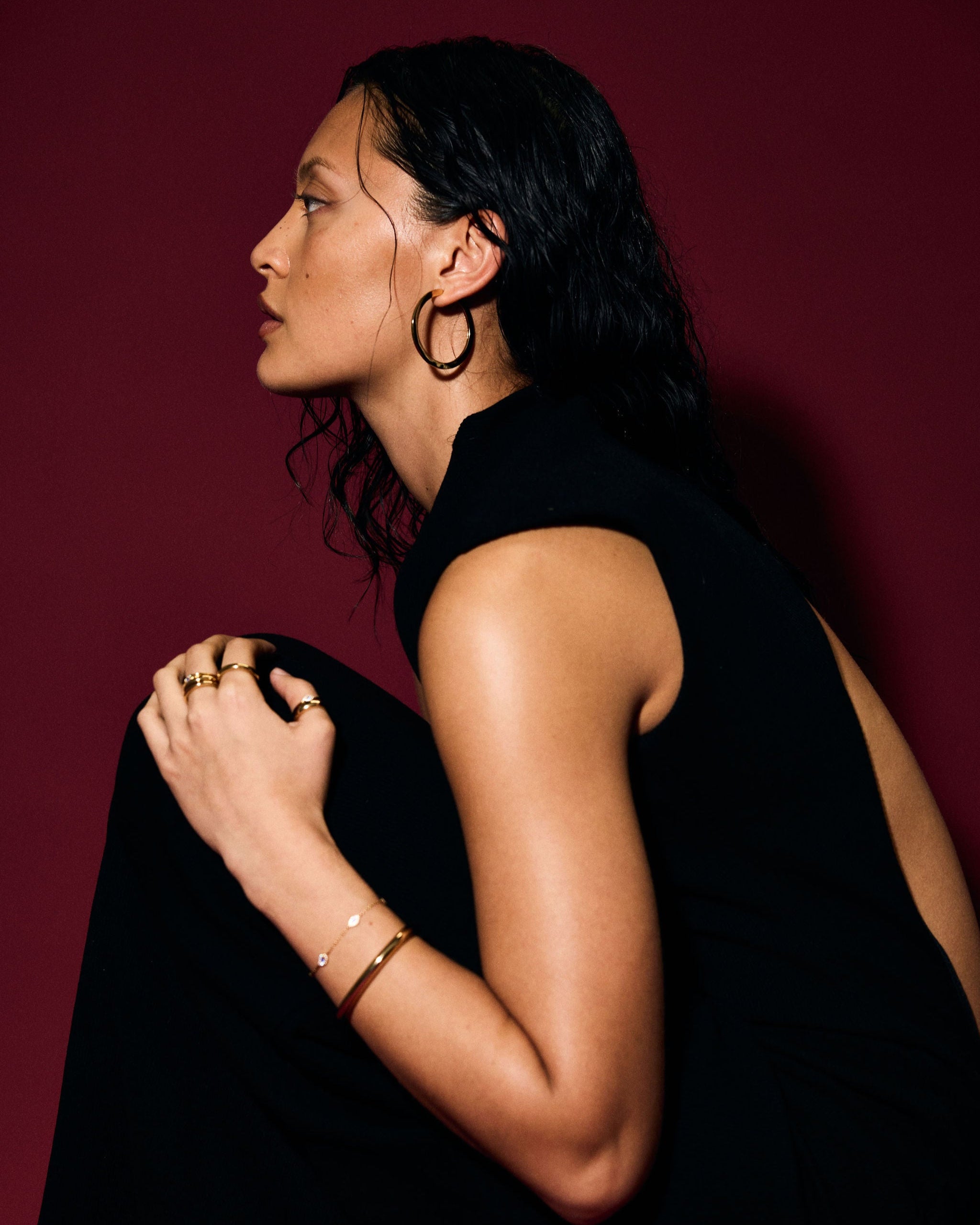 Woman in a black sleeveless top against a red background wearing a gold bangle