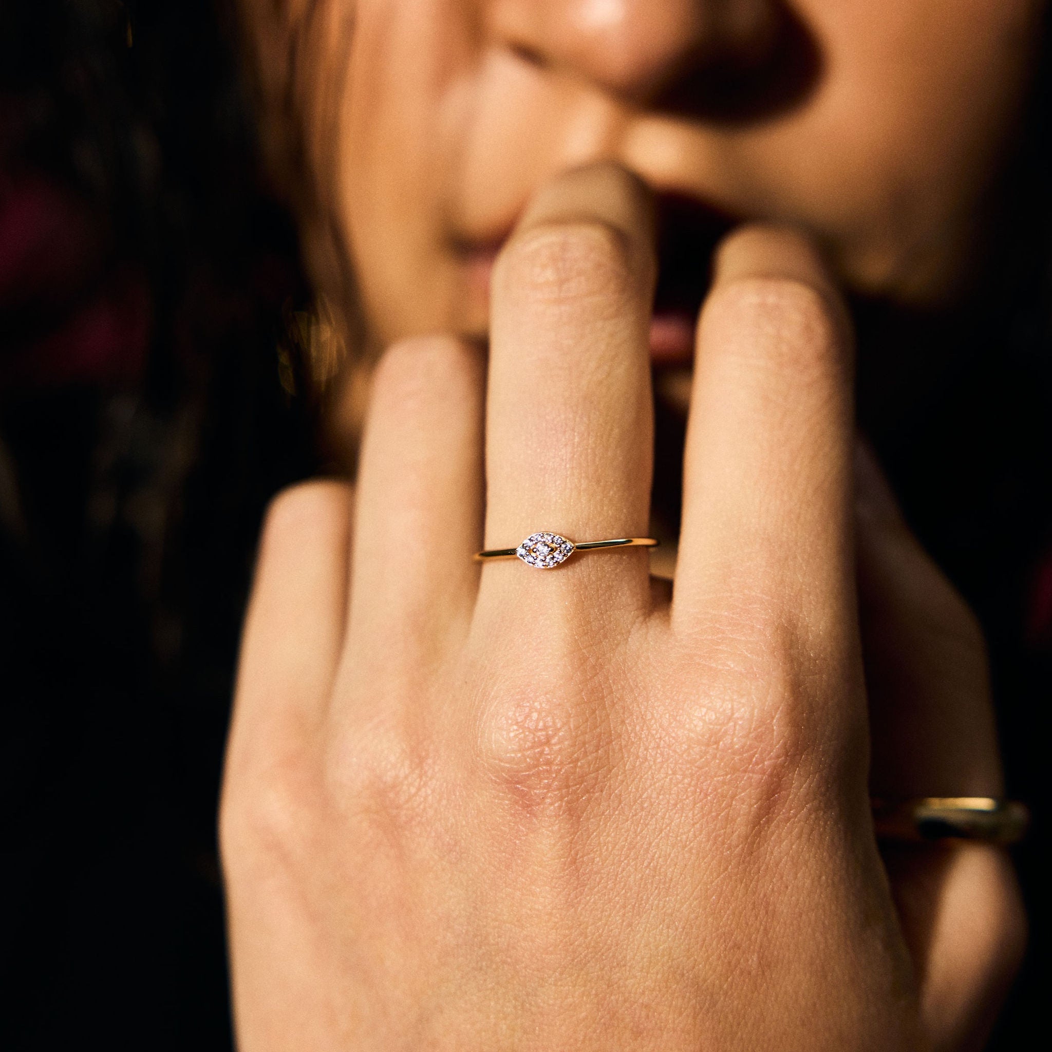 Close-up of a hand with clear stone evil eye ring on a dark background