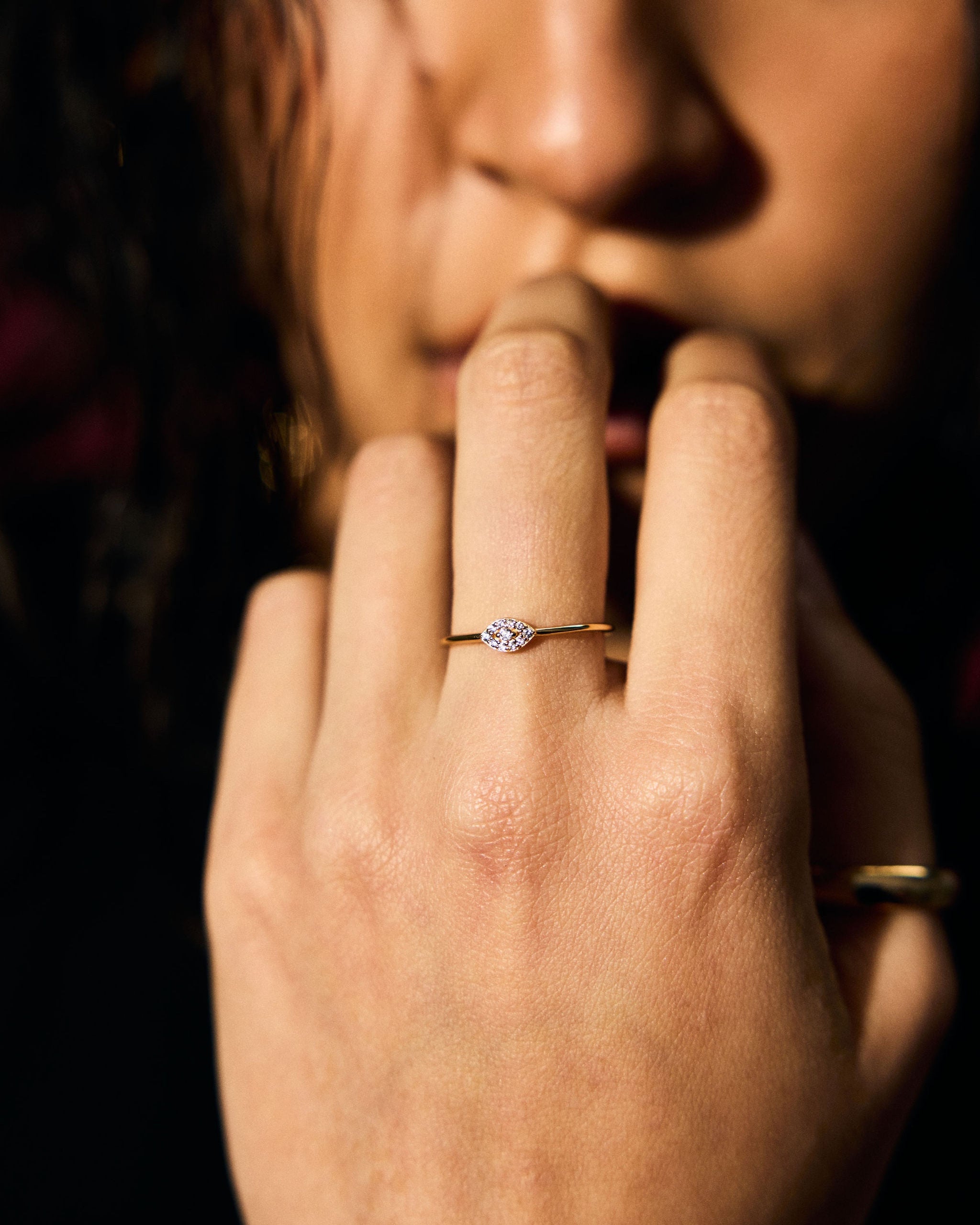 Close-up of a hand with clear stone evil eye ring on a dark background