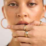 Close-up of a woman's face with gold rings on her fingers against a neutral background