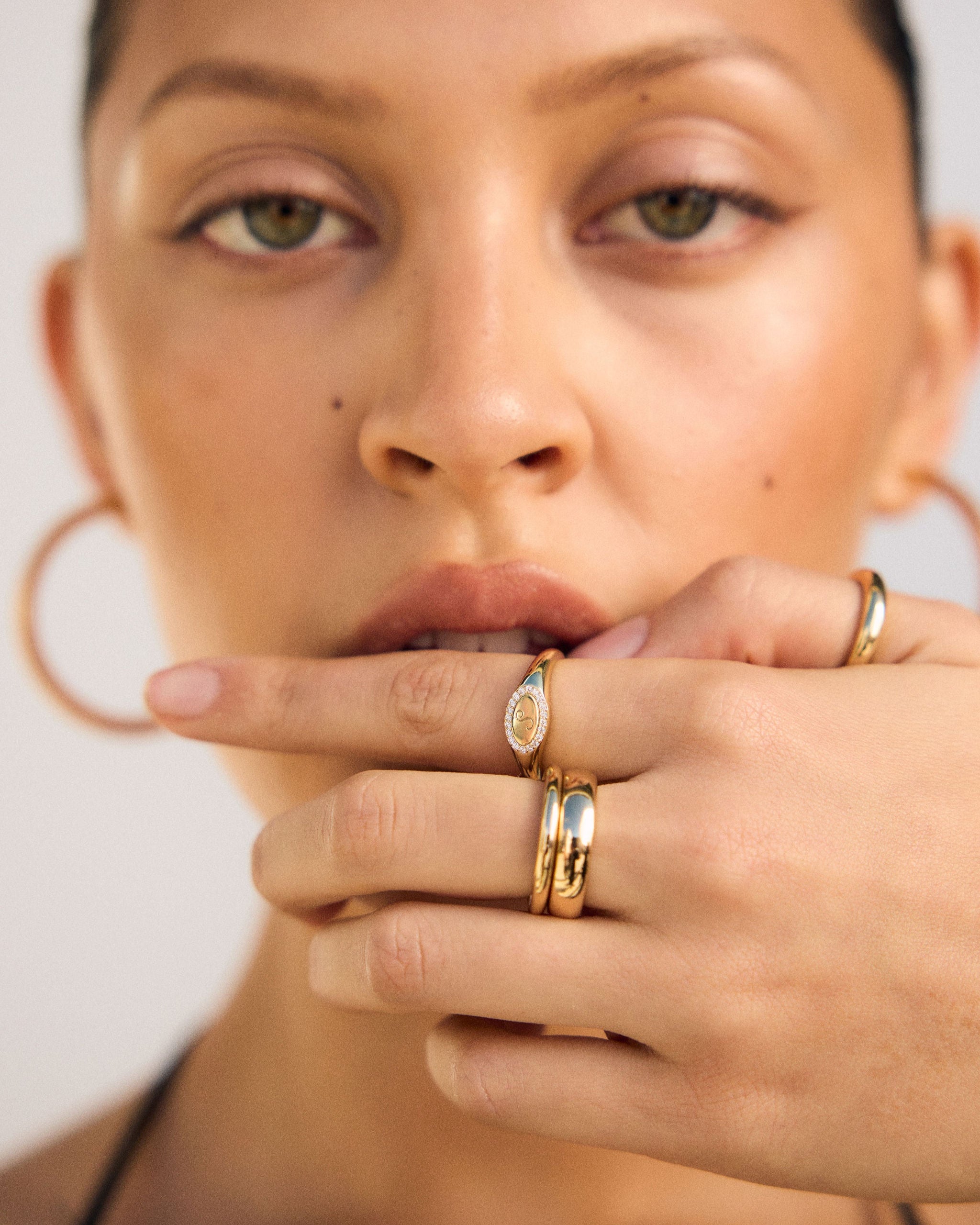 Close-up of a woman's face with gold rings on her fingers against a neutral background