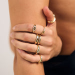 Close-up of a hand wearing multiple gold rings on a neutral background