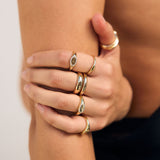 Close-up of a hand wearing multiple gold rings on a neutral background
