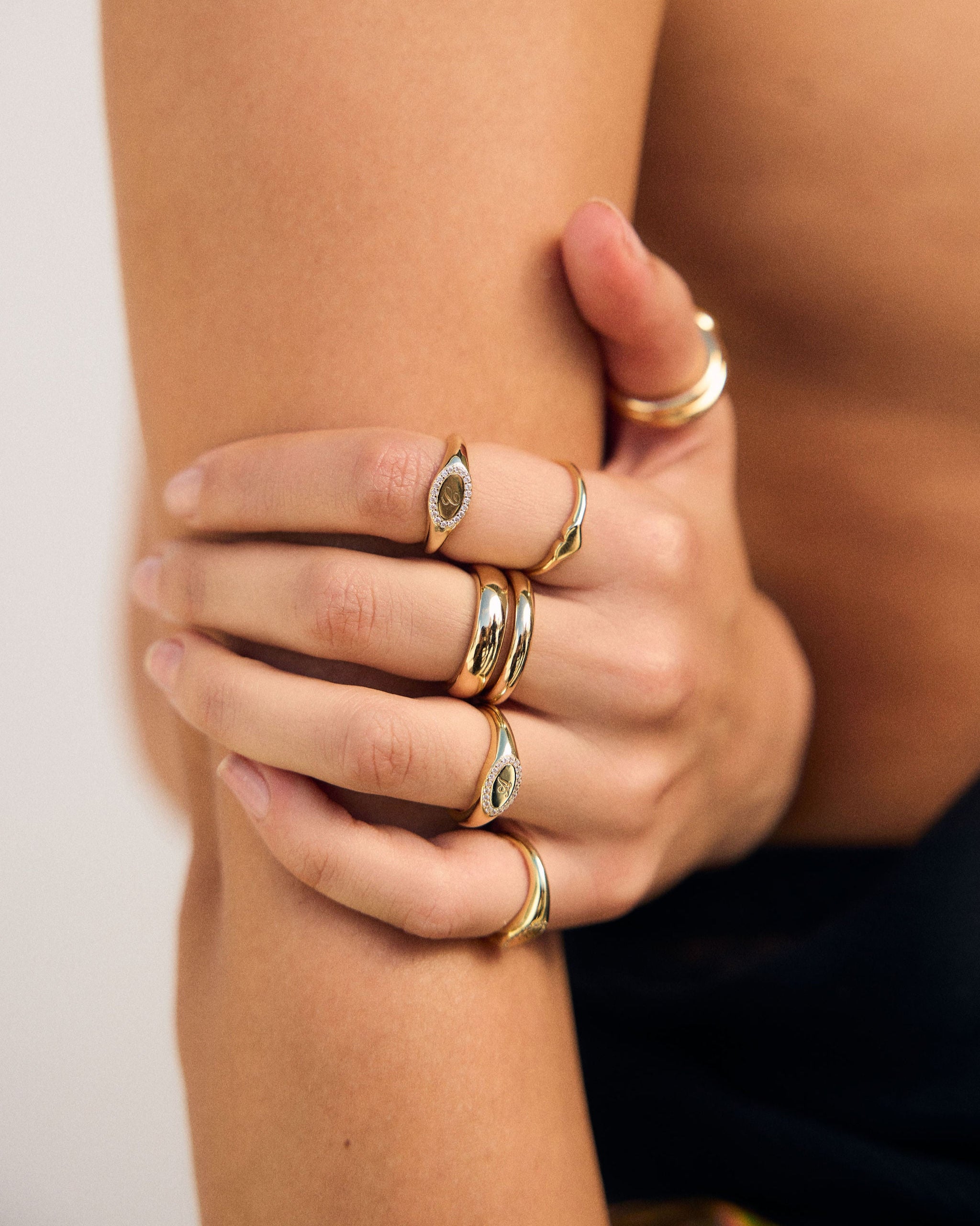 Close-up of a hand wearing multiple gold rings on a neutral background