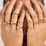 Close-up of hands wearing multiple gold rings with gemstones.