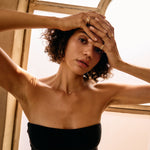 Woman in a black dress with hands on head in front of a window