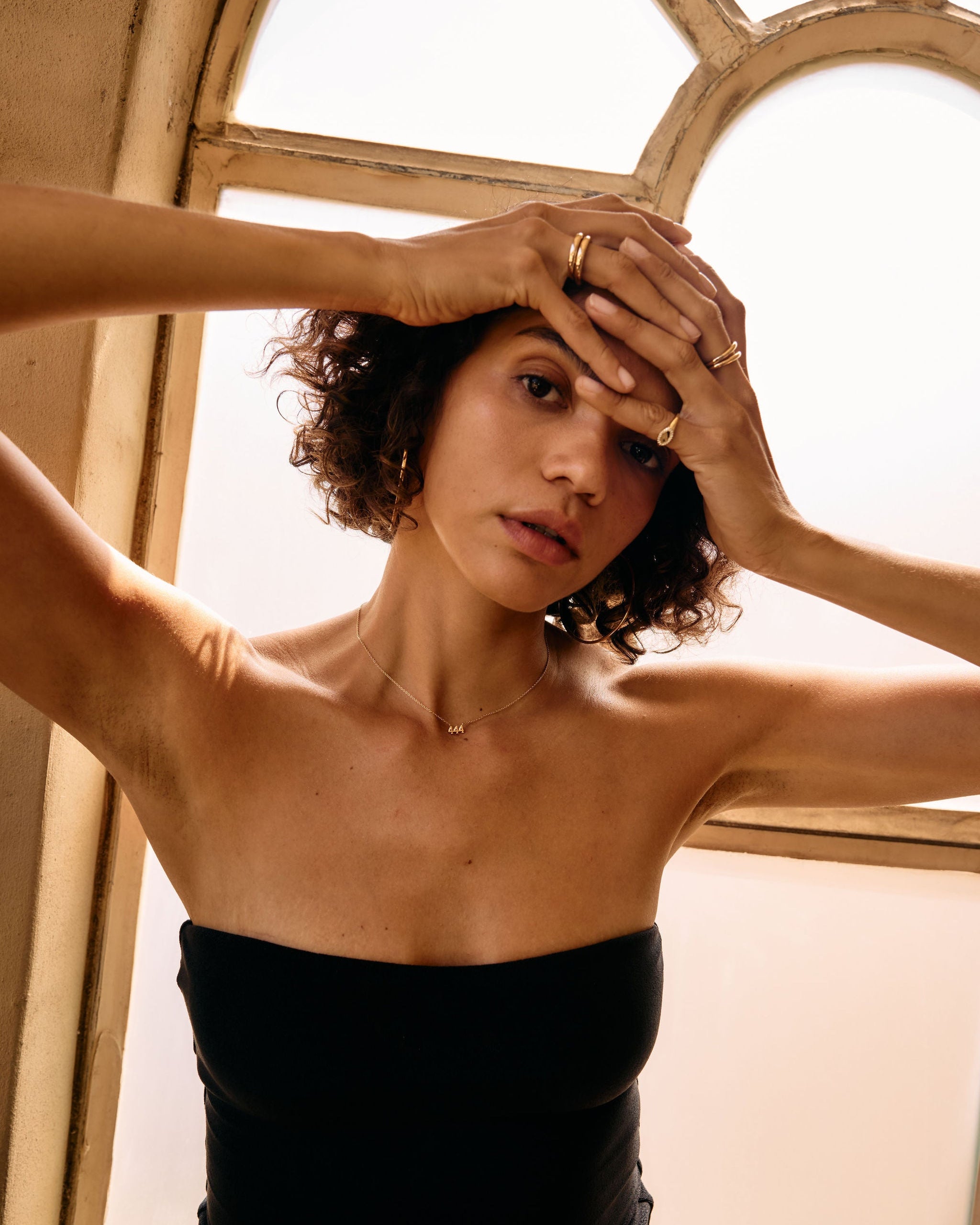 Woman in a black dress with hands on head in front of a window