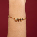 Gold bracelet with heart-shaped charms on a wrist against a red background