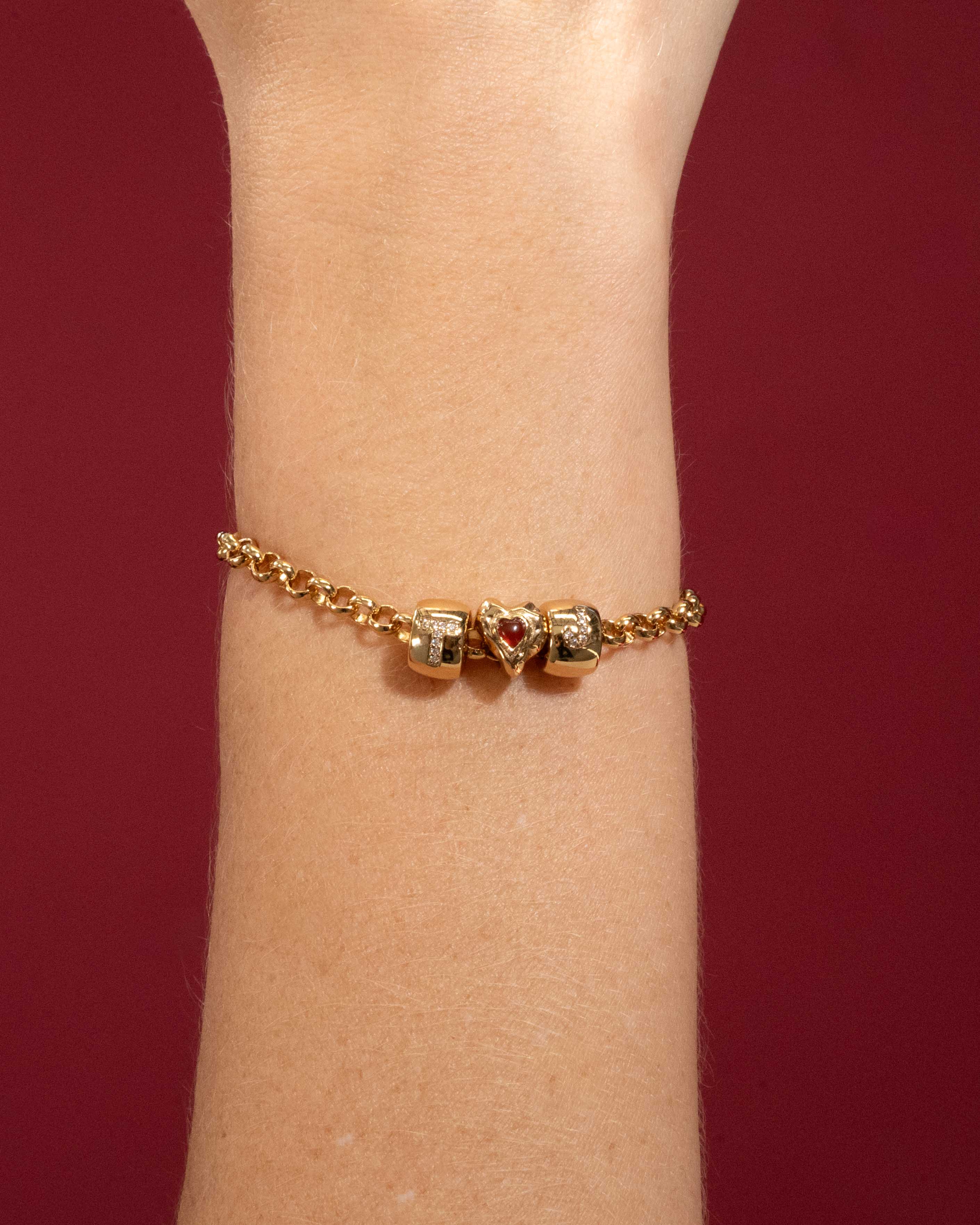 Gold bracelet with heart-shaped charms on a wrist against a red background