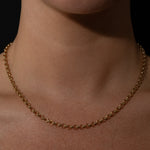 Gold belcher necklace on a person's neck against a dark background