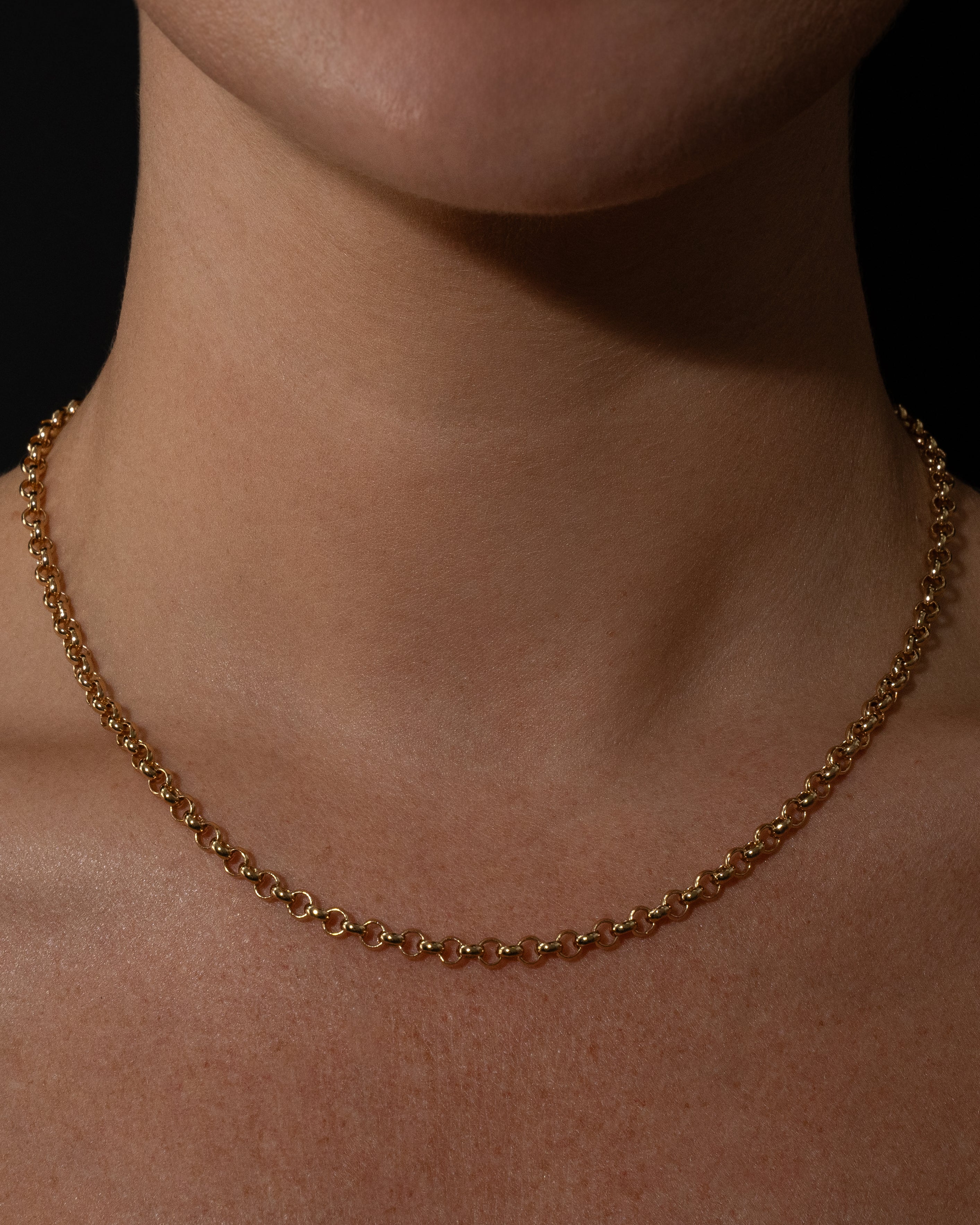 Gold belcher necklace on a person's neck against a dark background