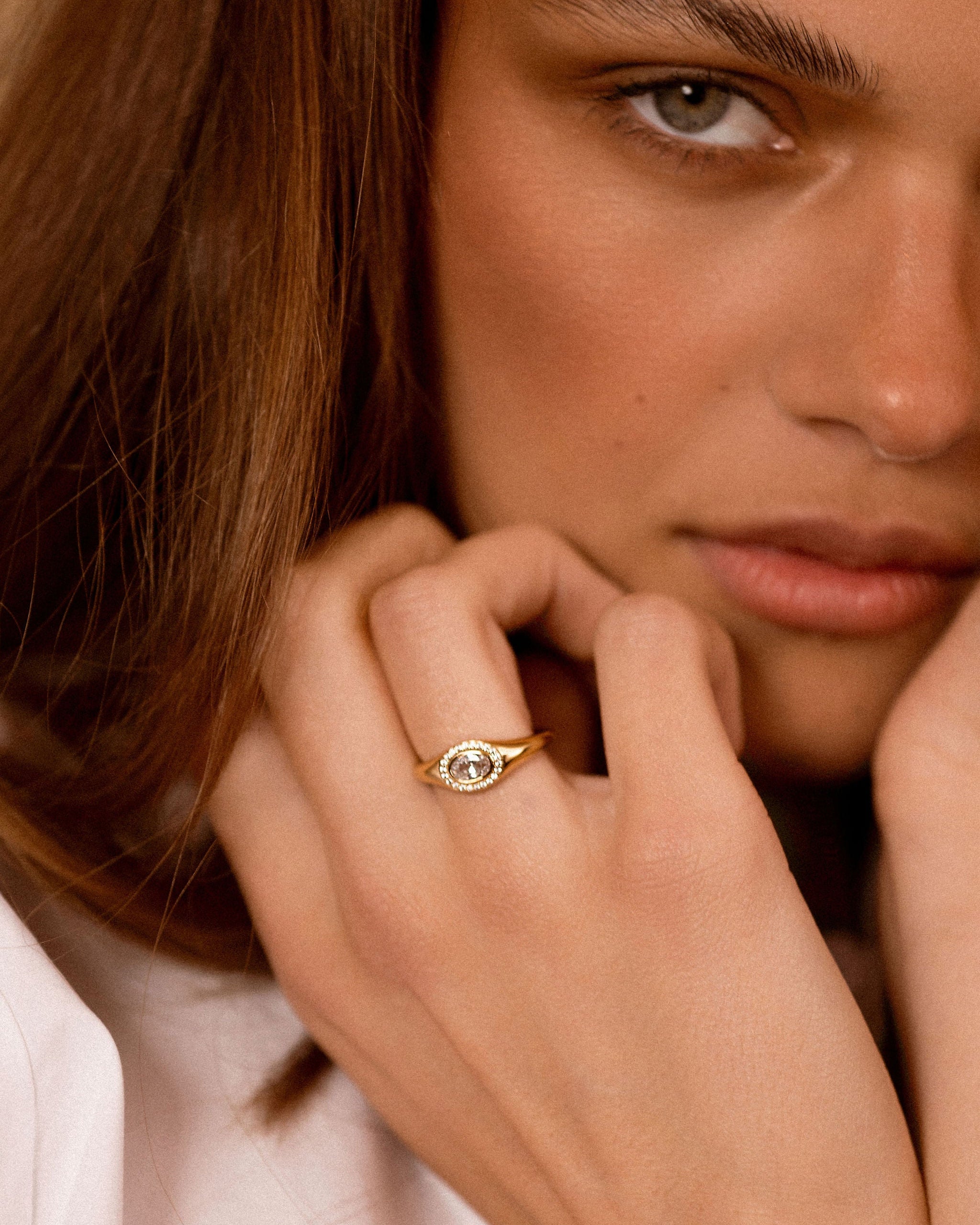 A close-up lifestyle shot of a woman wearing a delicate gold ring with a central oval-cut clear gemstone on her finger.