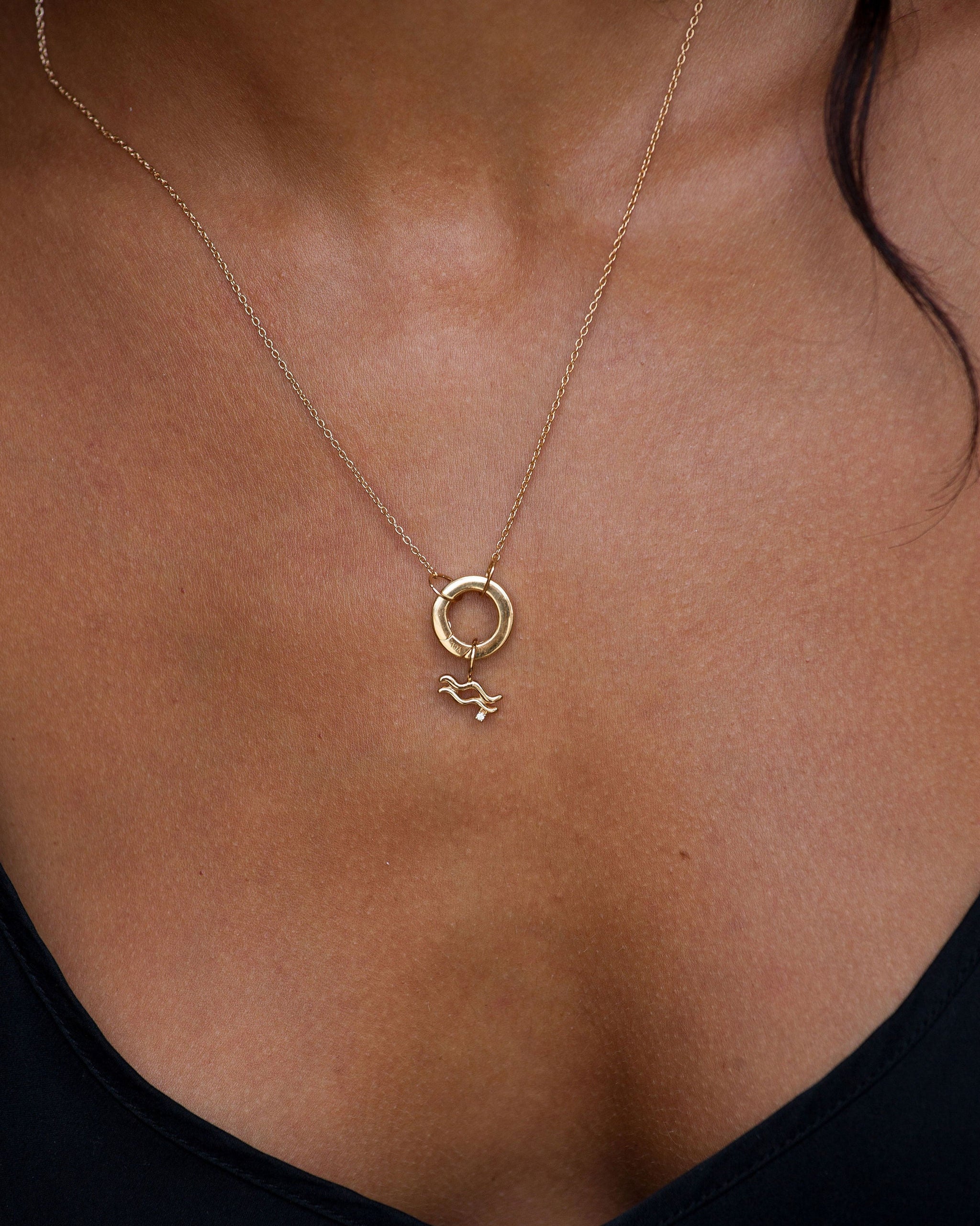 Gold necklace with a small pendant on a person wearing a black top.
