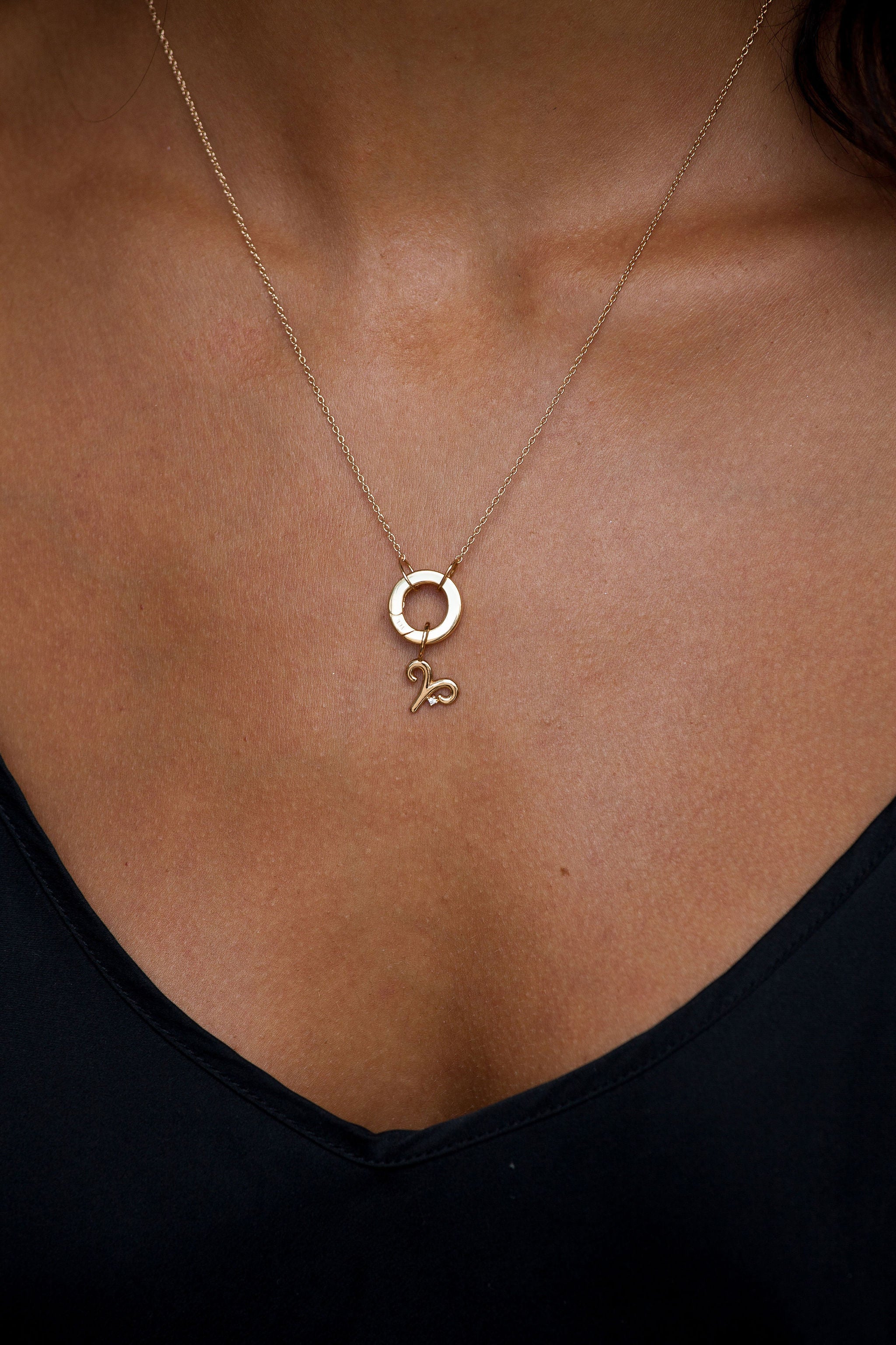 Gold necklace with a pendant on a person wearing a black top.