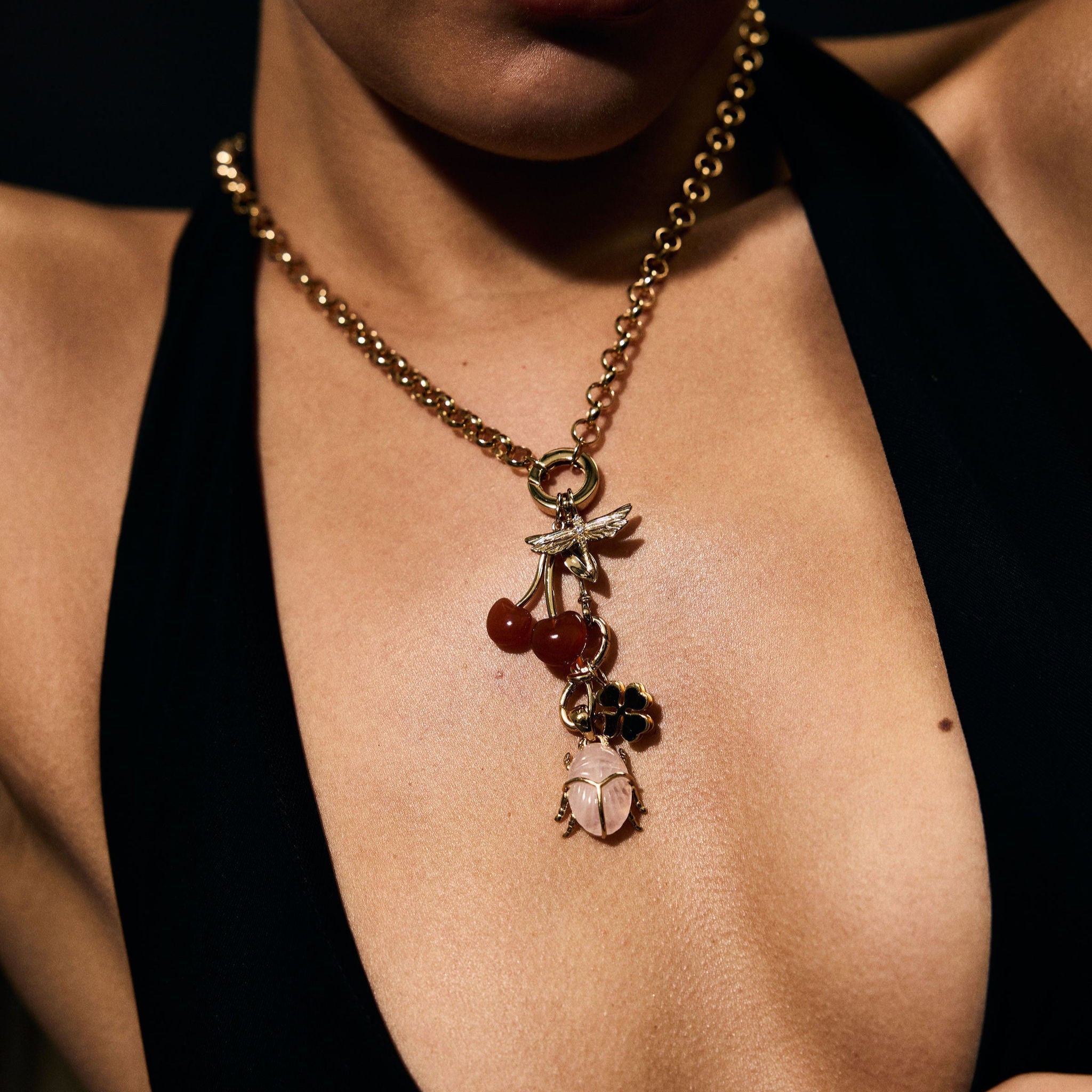 Close-up of a person wearing a gold necklace with charms against a dark background