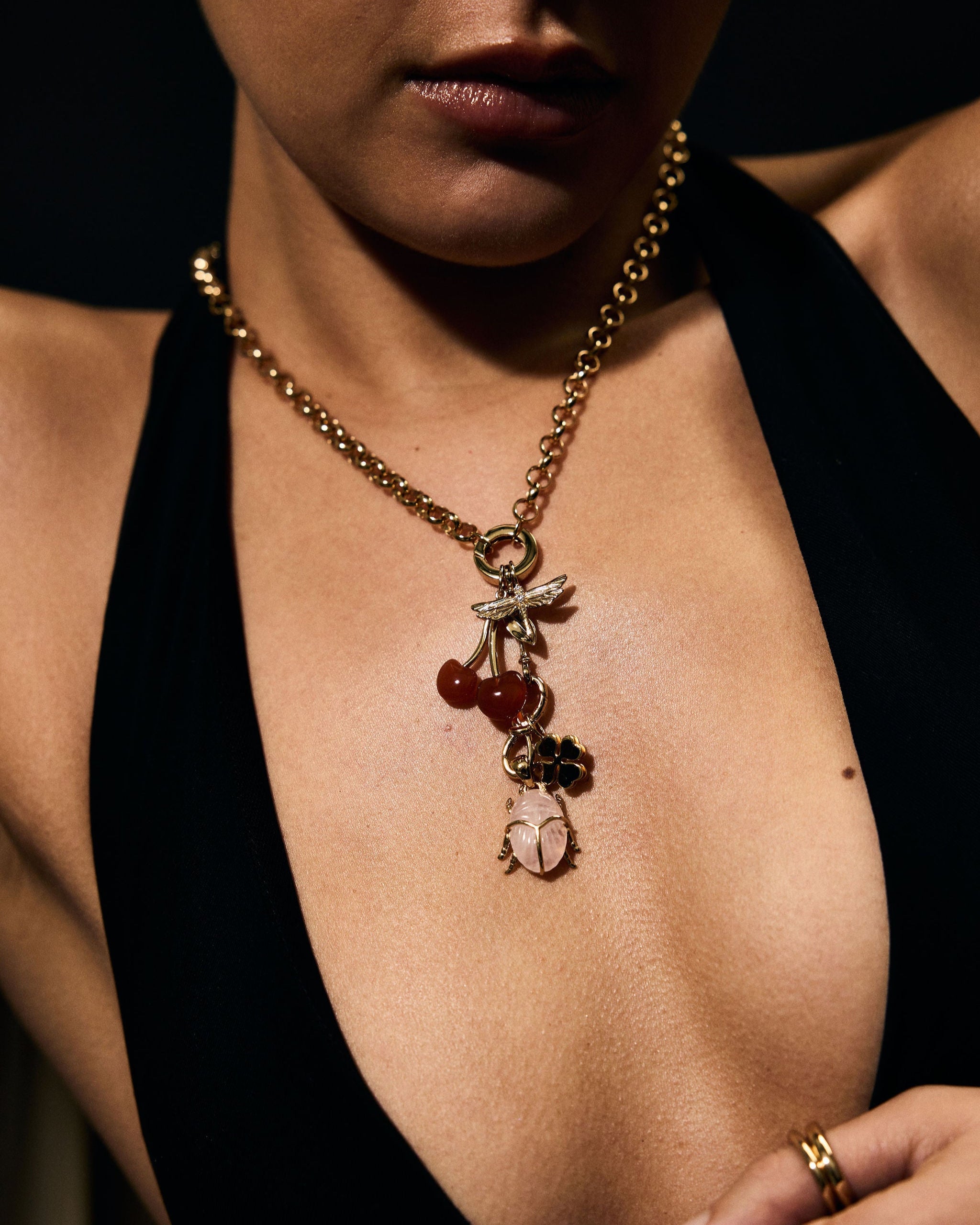 Close-up of a person wearing a gold necklace with charms against a dark background