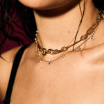 Close-up of a person wearing a gold evil eye necklace against a dark background