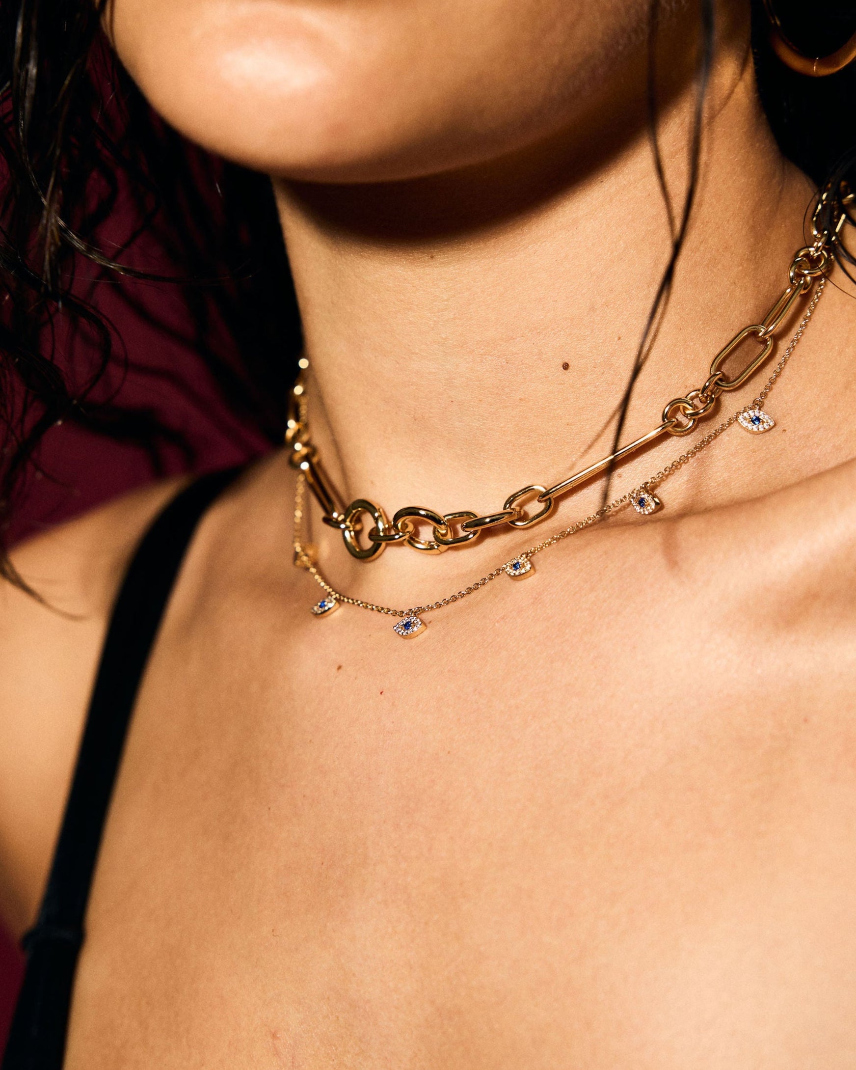 Close-up of a person wearing a gold evil eye necklace against a dark background