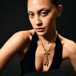 Woman wearing a black dress and gold necklace against a dark background