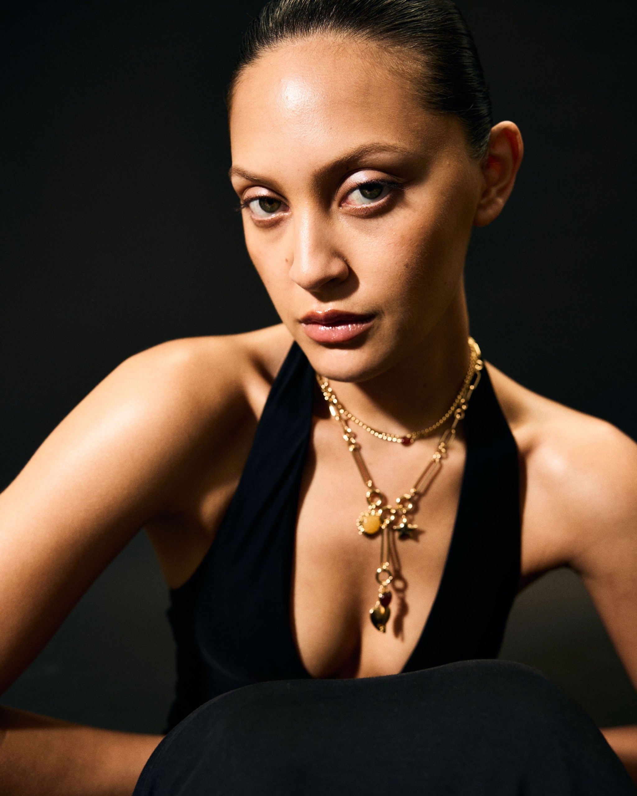 Woman wearing a black dress and gold necklace against a dark background