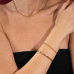 Person wearing a gold necklace and bracelet on a red background