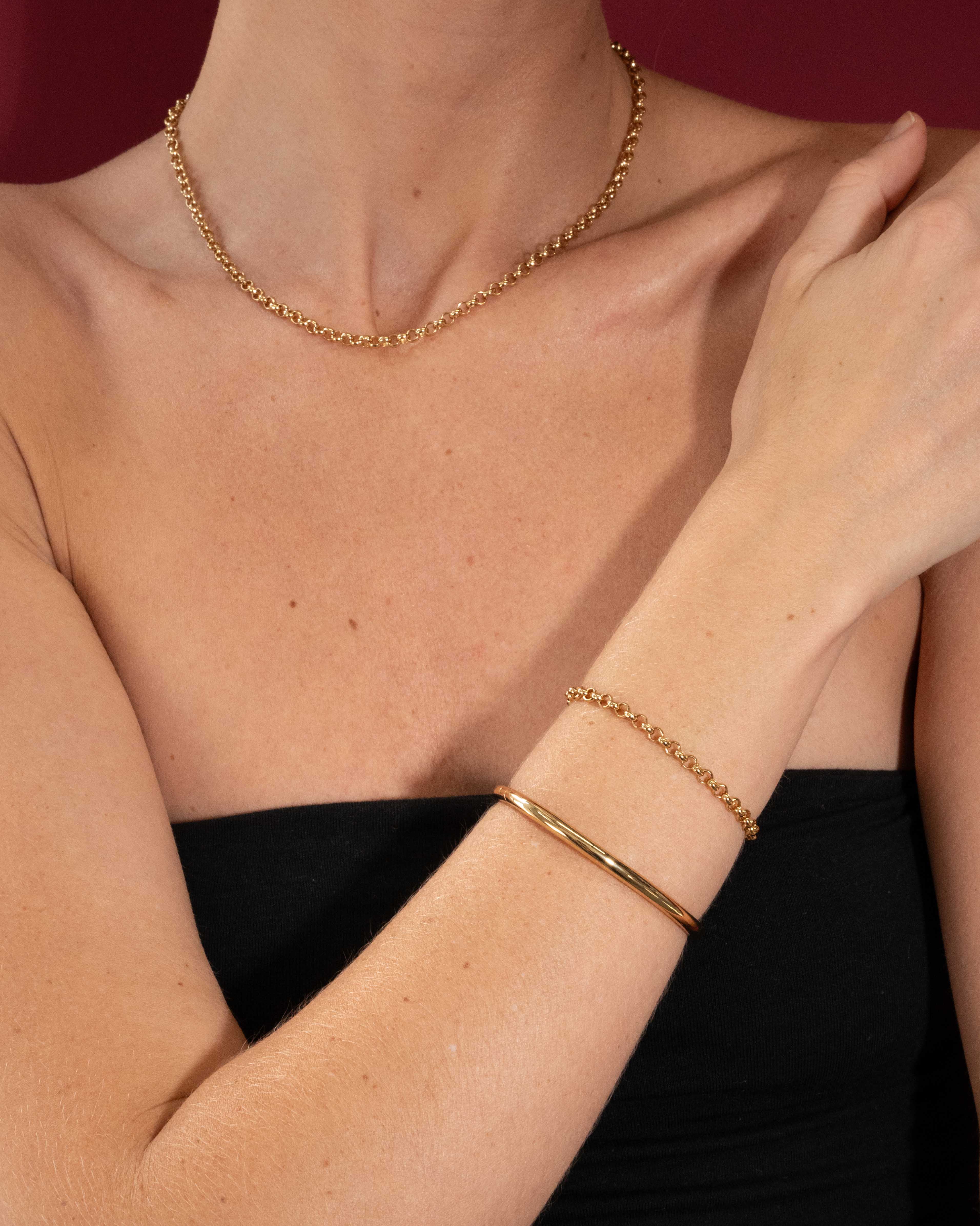 Person wearing a gold necklace and bracelet on a red background