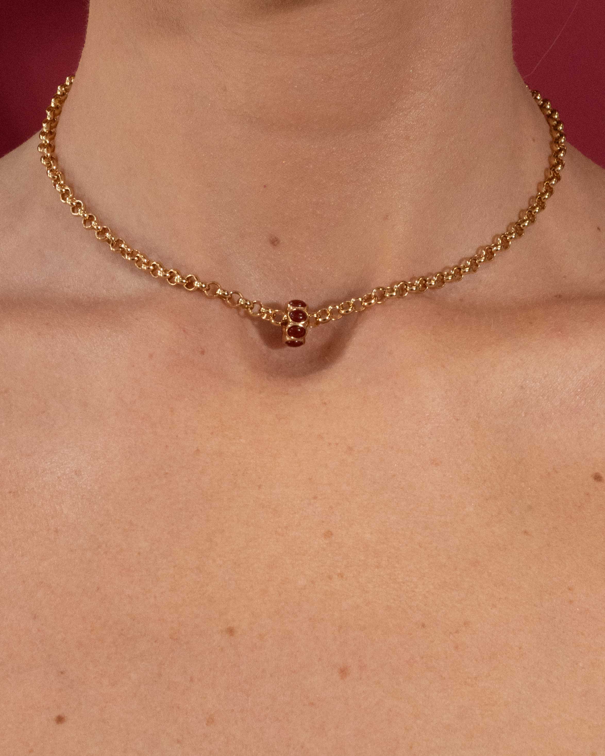Gold necklace on a person's neck with a red background