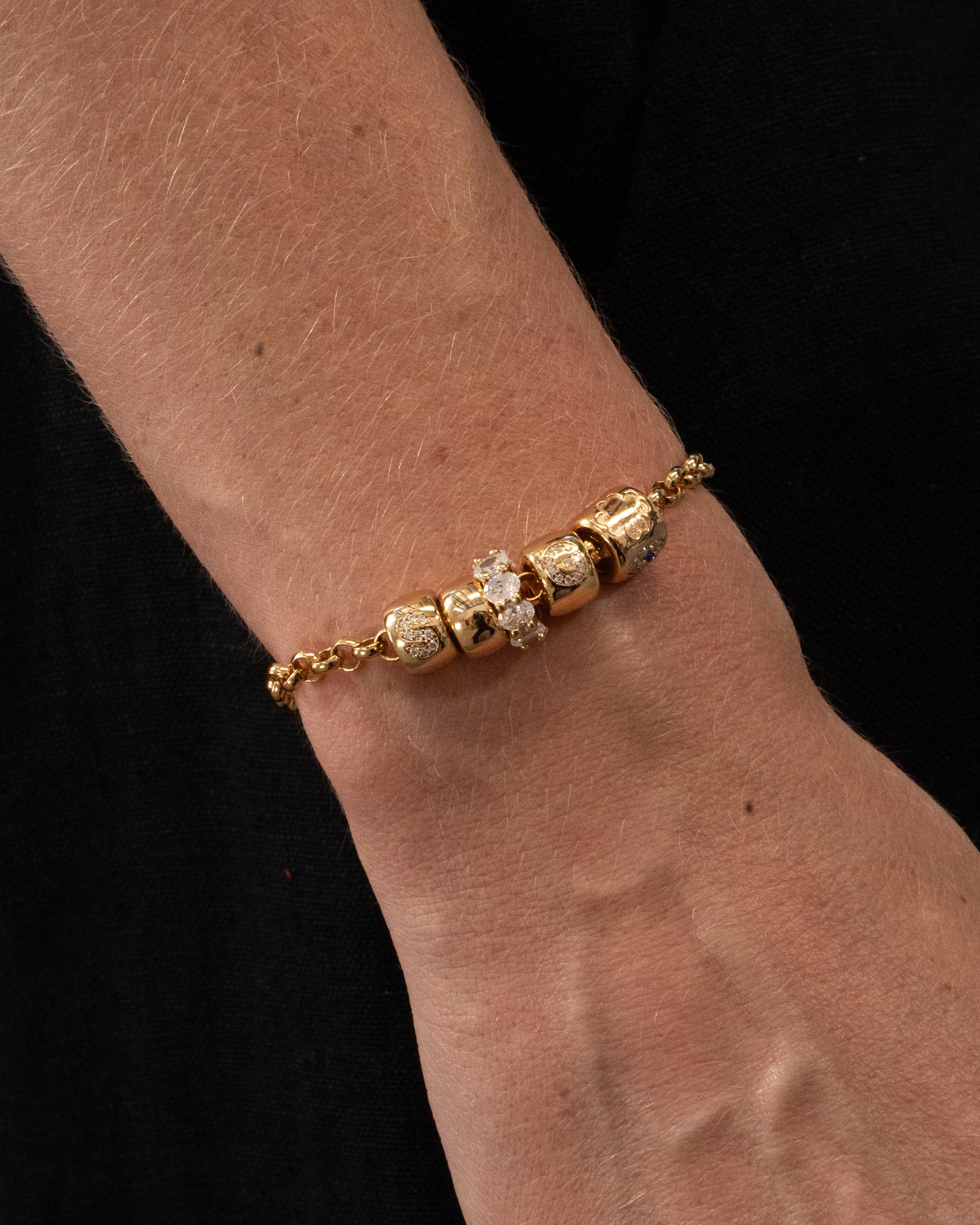 Gold bracelet with diamond beads on a wrist against a black background
