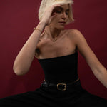 Woman in a black dress with a gold belt against a red background