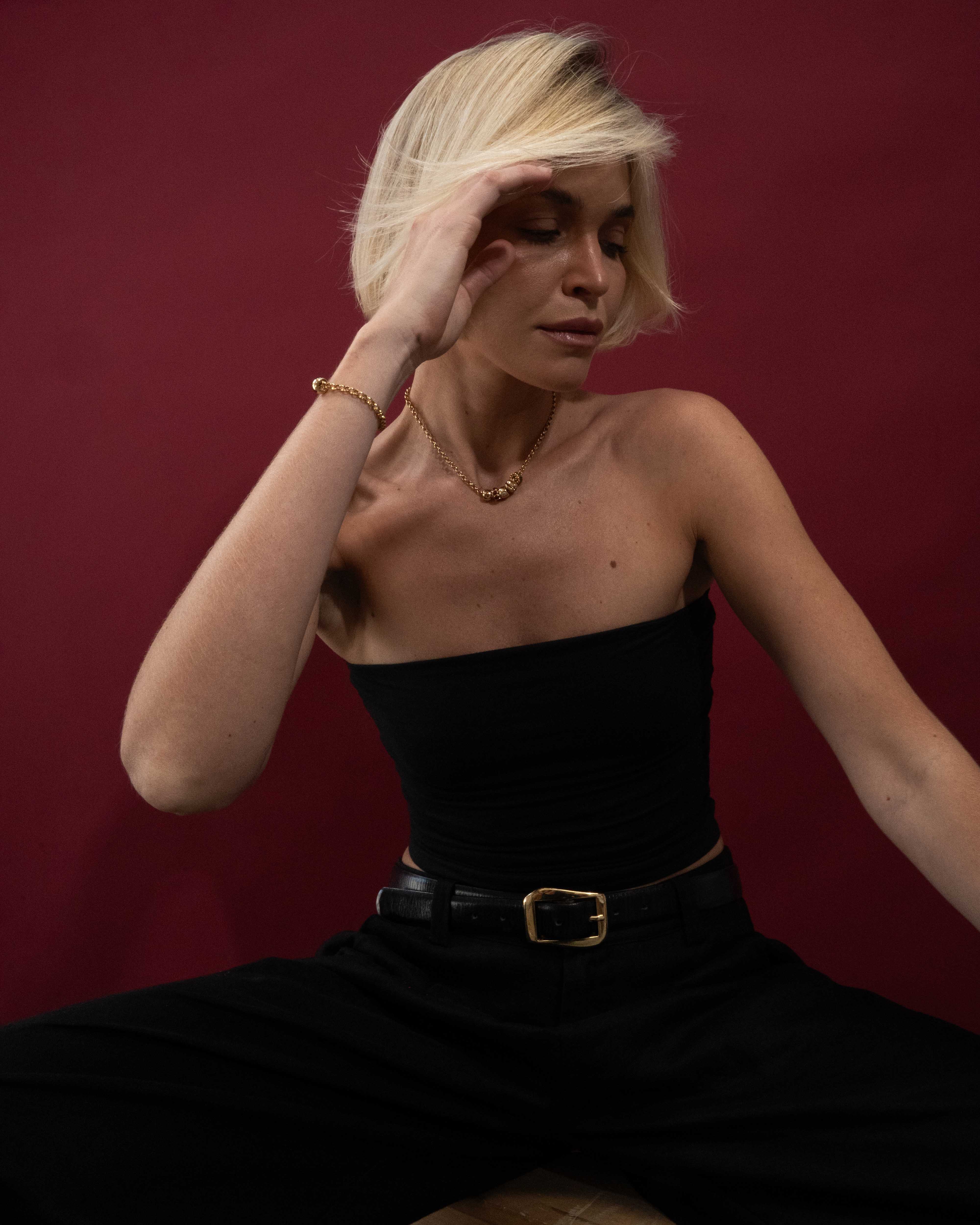Woman in a black dress with a gold belt against a red background