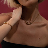 Person wearing a gold necklace and bracelet against a red background