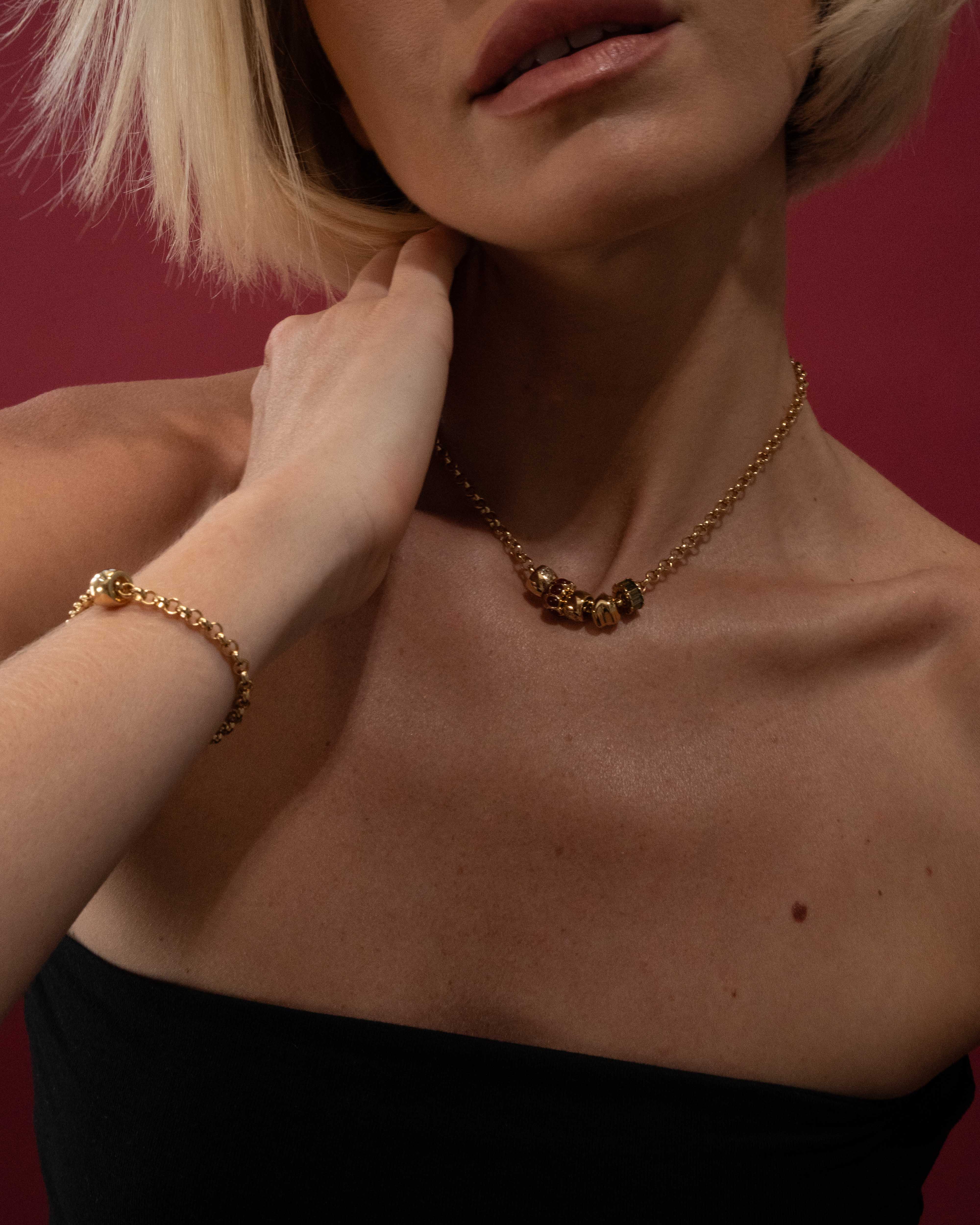 Person wearing a gold necklace and bracelet against a red background
