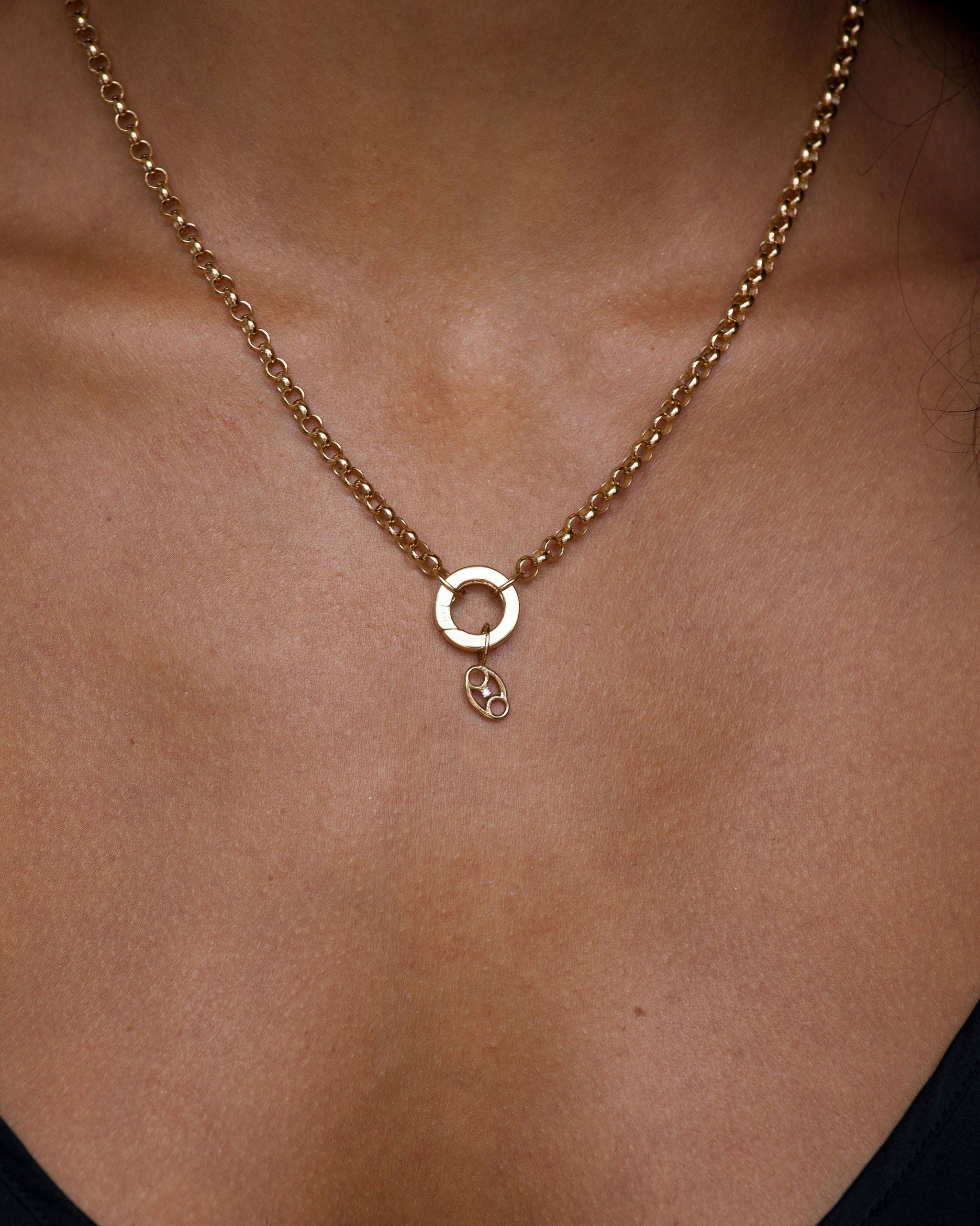 Gold necklace with a small pendant on a person wearing a black top.