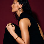 Woman in a black sleeveless top against a red background wearing a gold bangle