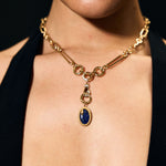 Close-up of a person wearing a gold necklace with a blue pendant against a black background