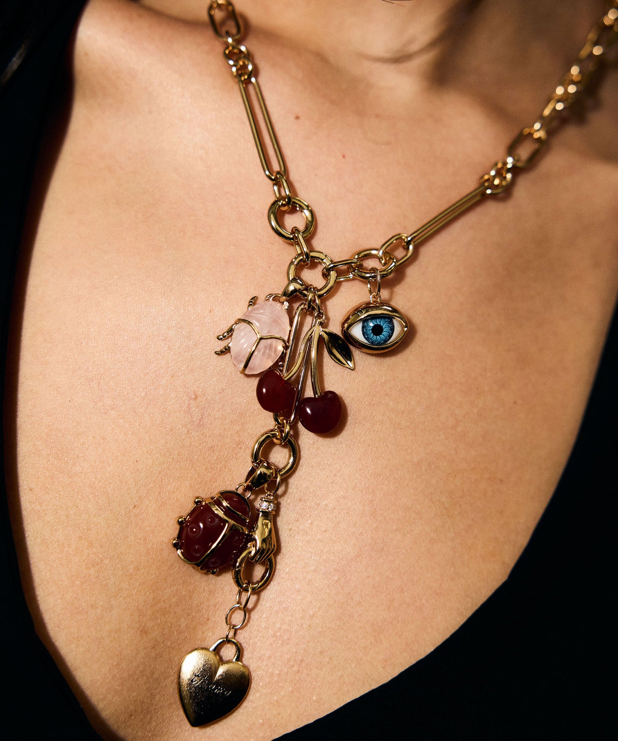 Gold necklace with various charms on a person wearing a black top.