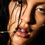 Close-up of a woman's face with a fine gold evil eye necklace draped over her lips.
