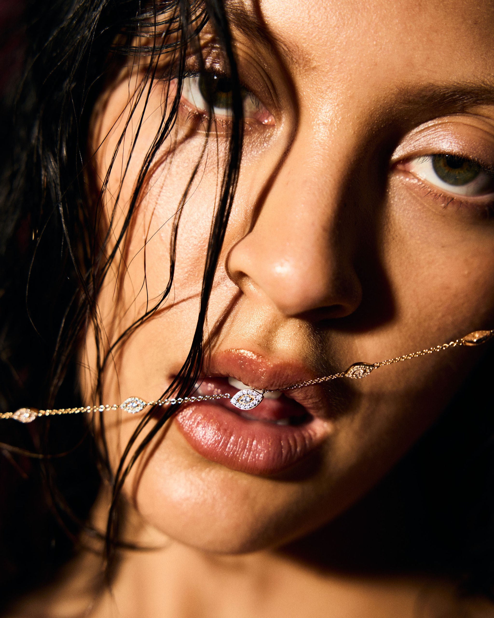 Close-up of a woman's face with a fine gold evil eye necklace draped over her lips.