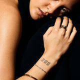 Close-up of a person with tattoos on their arm and hand, wearing stacked rings. 