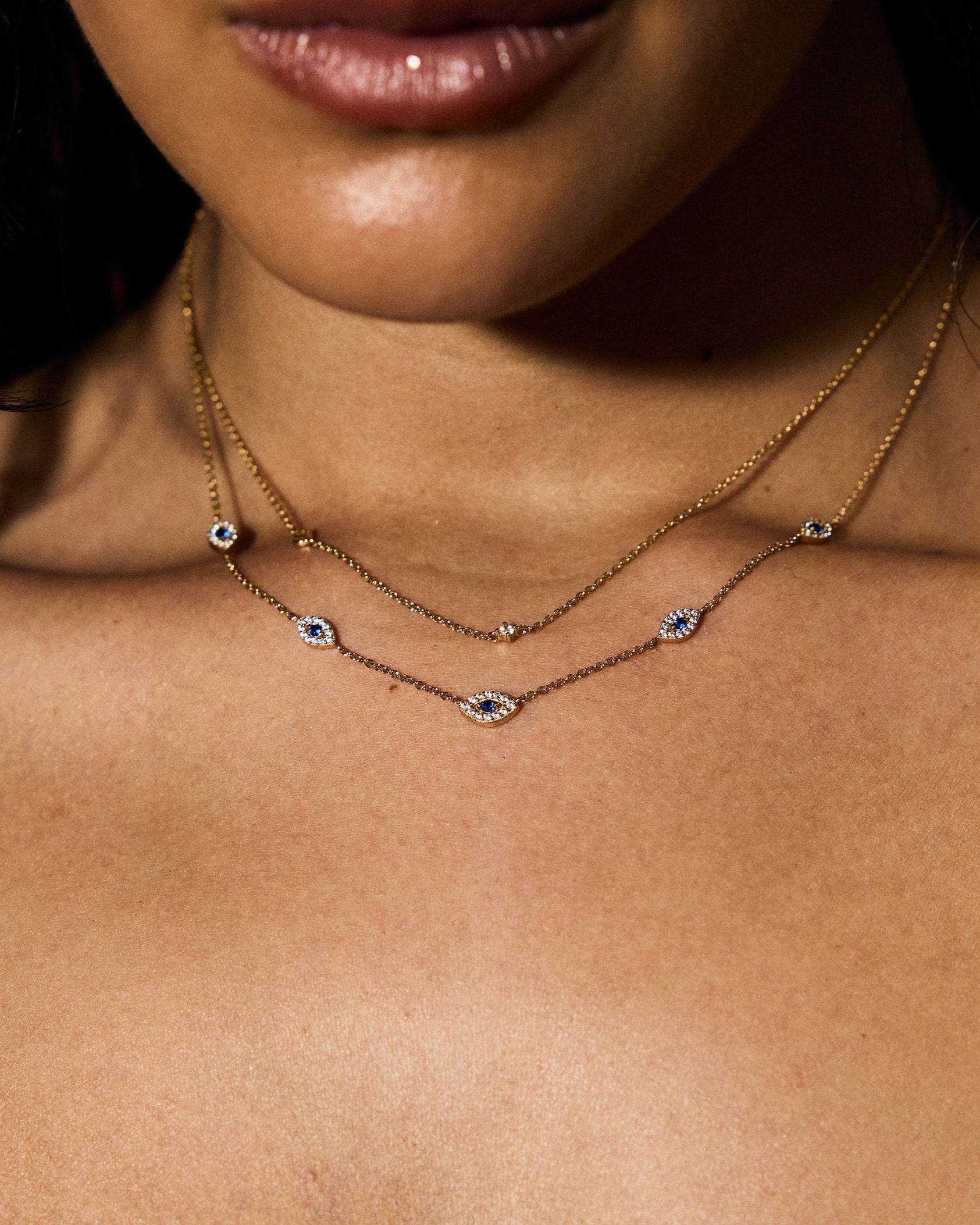 Close-up of a person wearing layered necklaces with eye-shaped pendants.