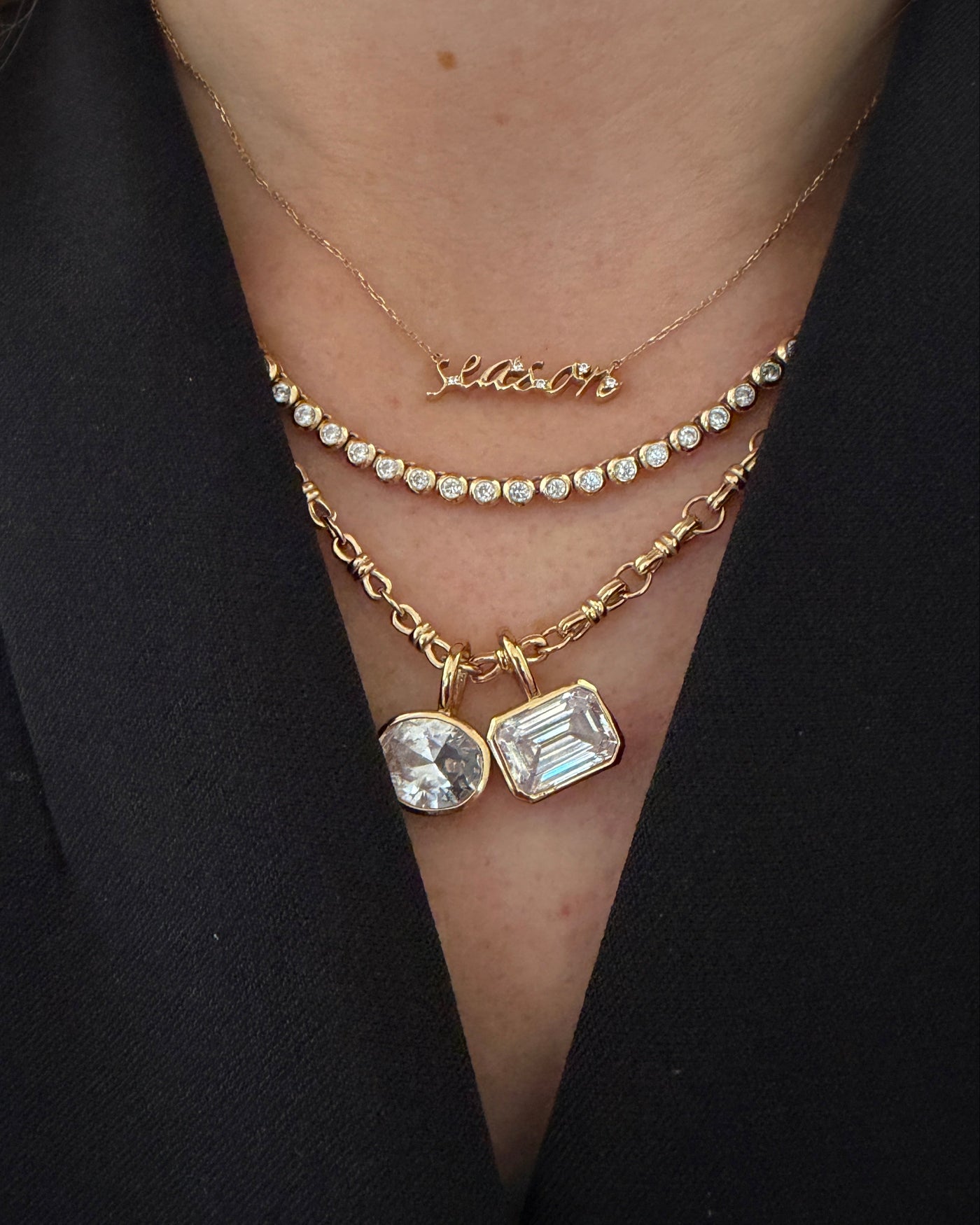 A close-up of a person's neck wearing multiple delicate gold bracelets, including a chain bracelet with clear stones and a pendant with an emerald-cut clear gemstone and a round clear stone.
