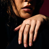 Close-up of a person with a hand resting on their face with a fine gold evil eye ring