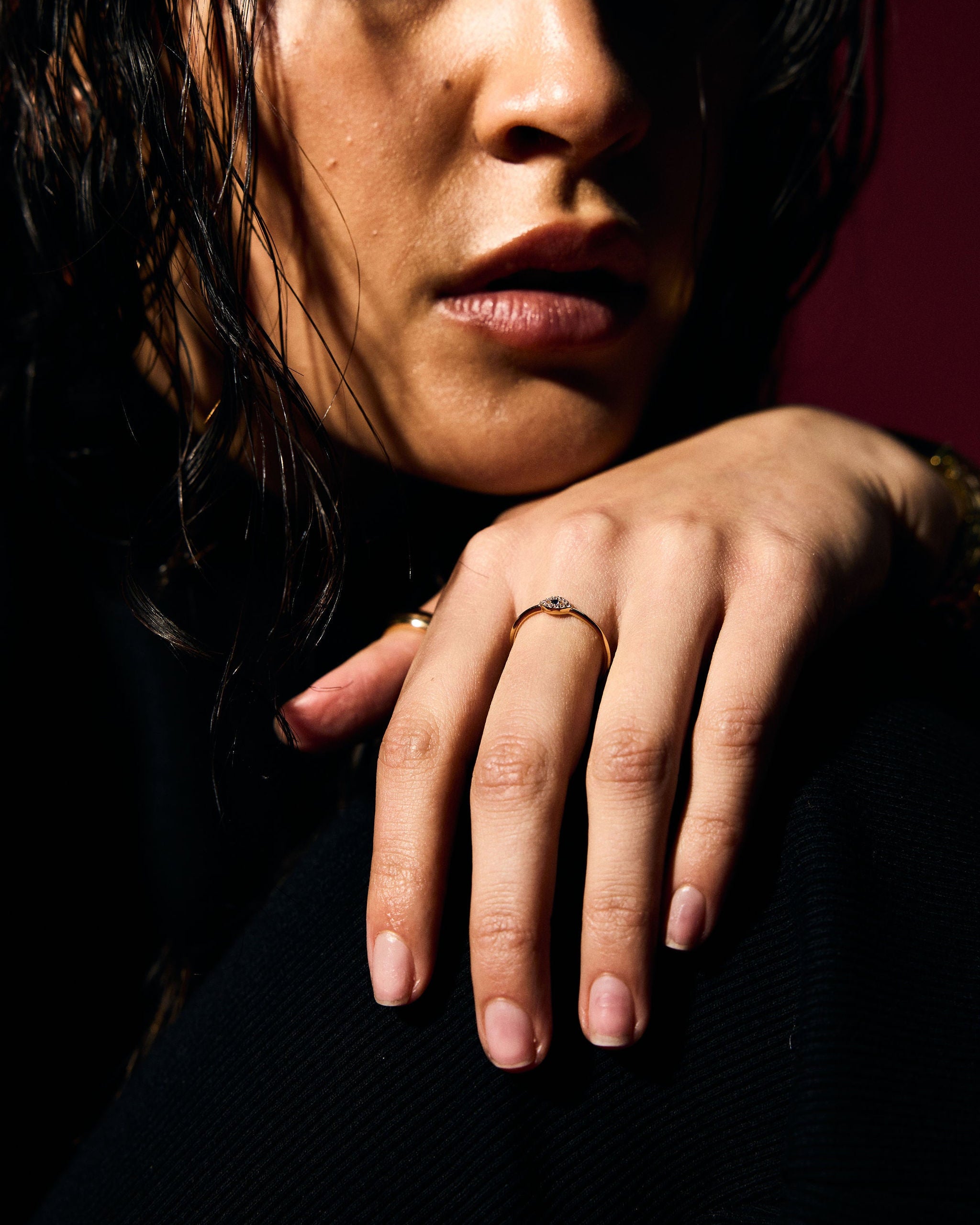 Close-up of a person with a hand resting on their face with a fine gold evil eye ring
