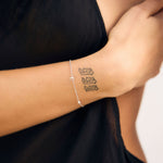 Person wearing a bracelet with a small tattoo on the wrist against a black background