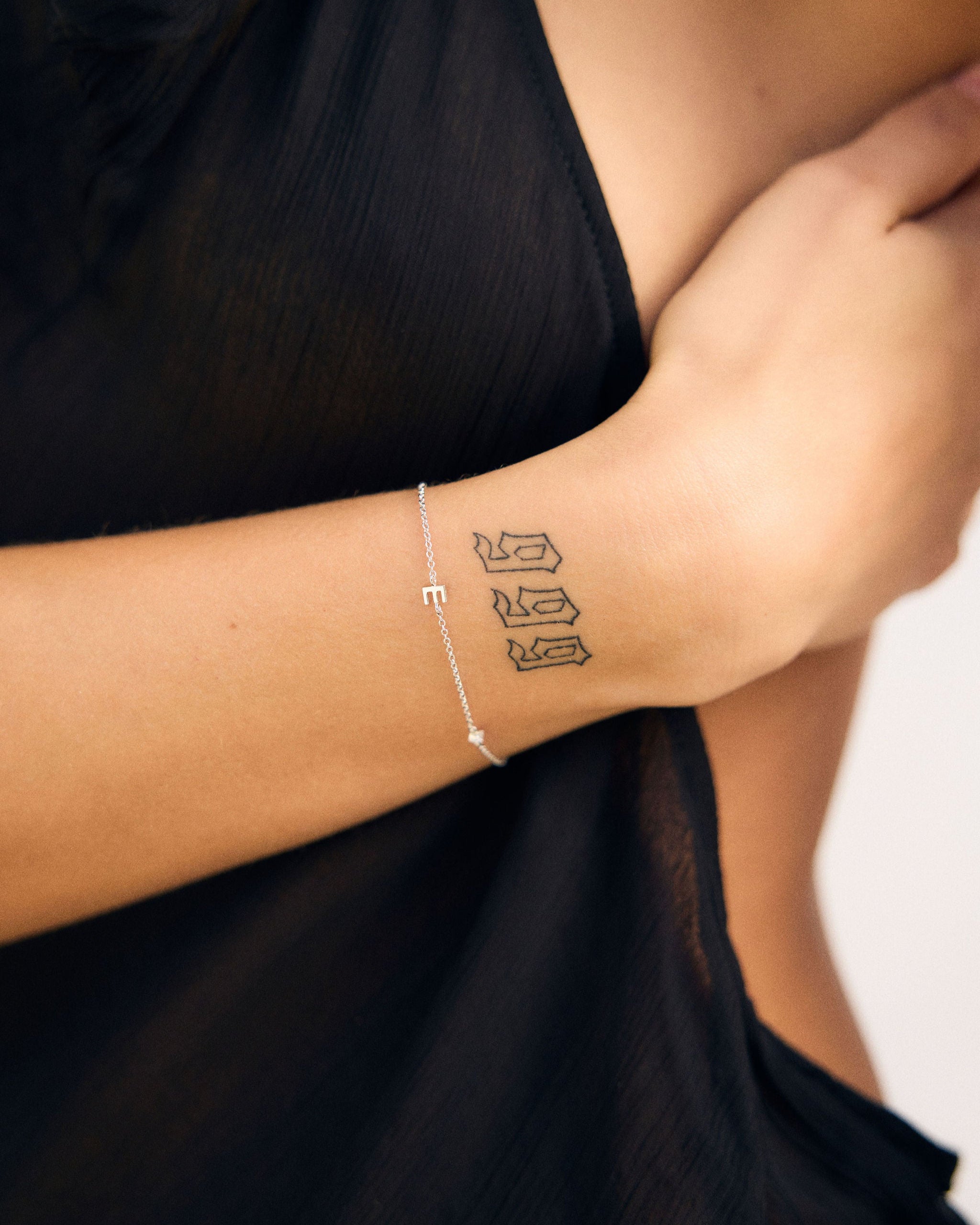 Person wearing a bracelet with a small tattoo on the wrist against a black background