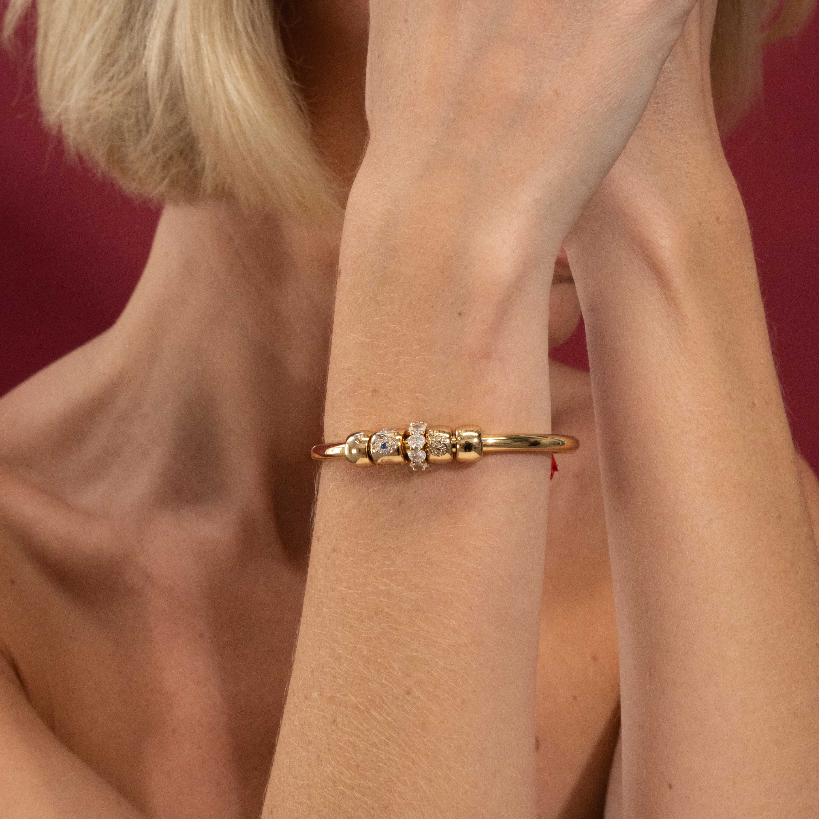 Gold bracelet with small diamonds on a person's wrist against a red background